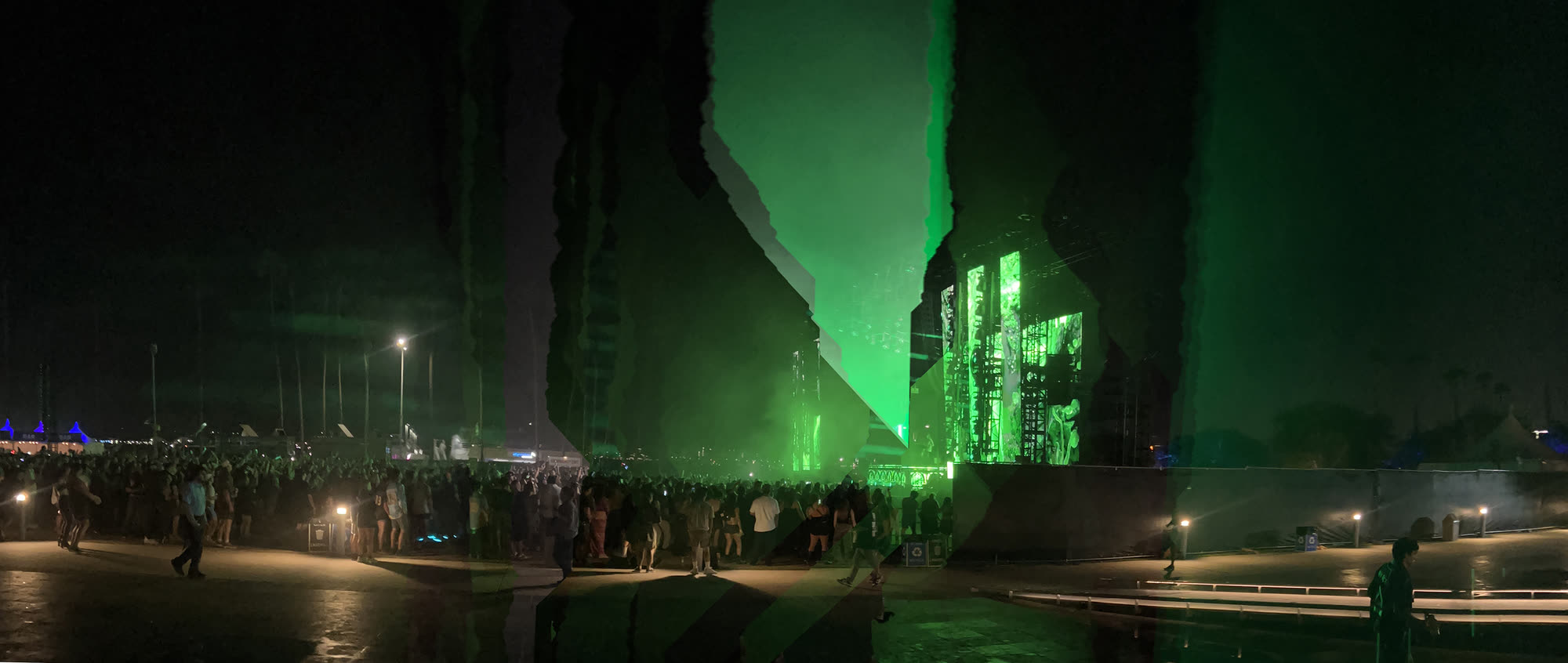 Green laser light across a crowd, split by a diagonal seam where the panoramic stitch failed to reconcile two moments.